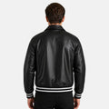 Person wearing a black leather jacket with white stripes on a plain background