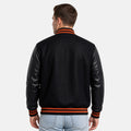Man wearing a black varsity jacket with leather sleeves on a white background