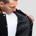 Stylish black varsity jacket with contrasting black leather sleeves and orange ribbed trim, perfect for a casual yet fashionable outfit