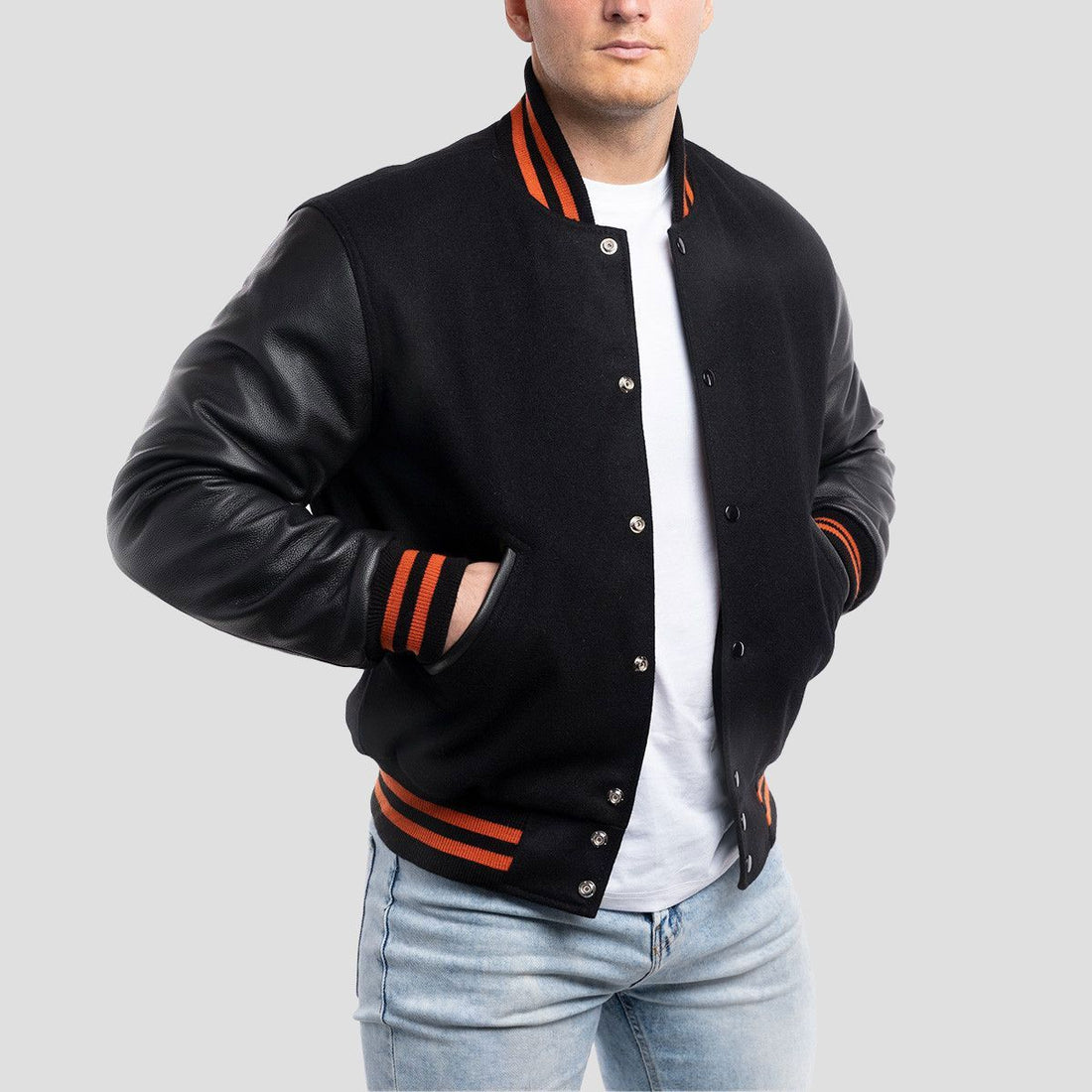 Men's black varsity jacket with black leather sleeves and vibrant orange ribbed trim, combining sporty style with modern flair