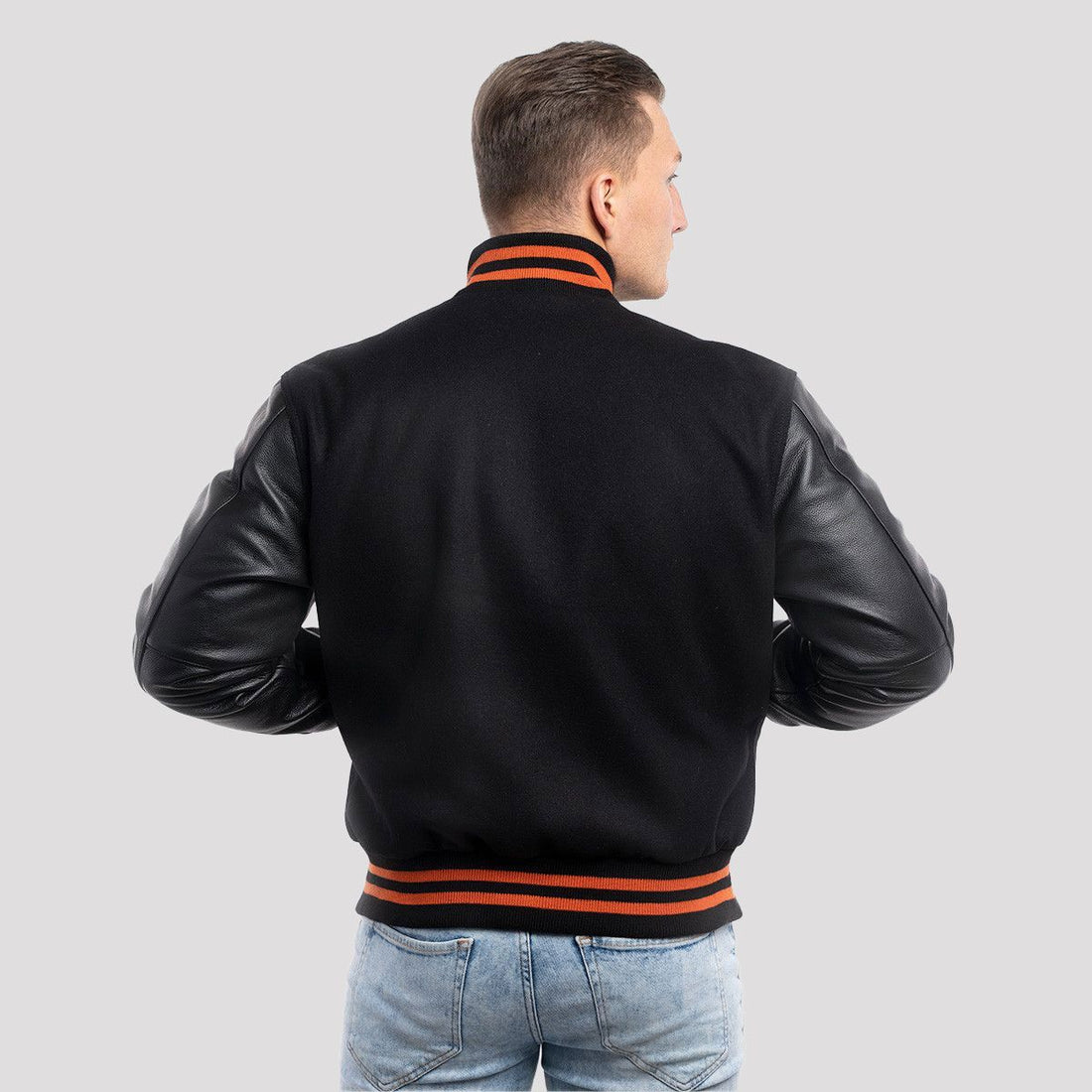 Men's black varsity jacket with black leather sleeves and vibrant orange ribbed trim, combining sporty style with modern flair