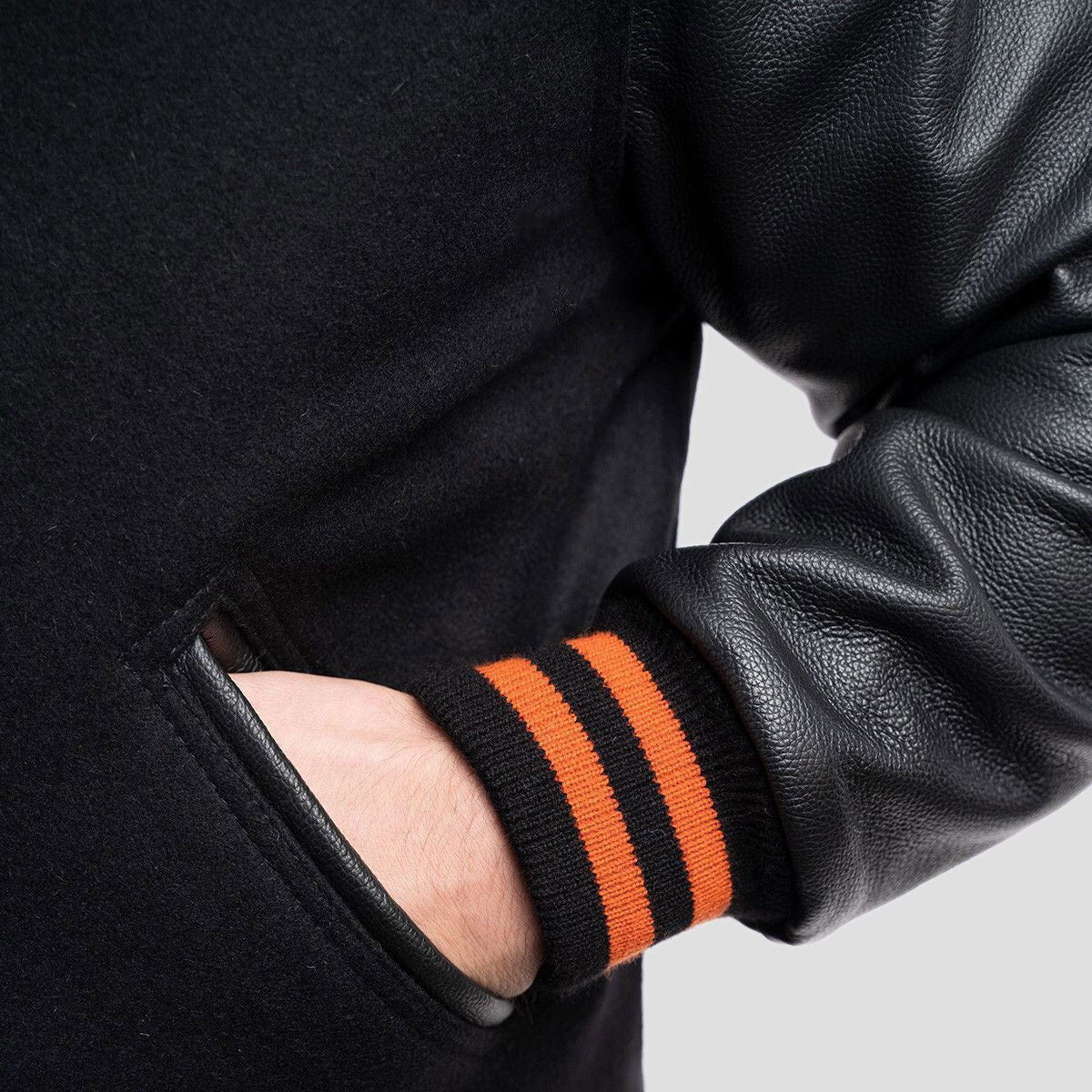 Classic black varsity jacket enhanced with black leather sleeves and bright orange ribbed accents, ideal for layering in any season