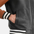 Close-up of a person wearing a black leather jacket with a brown sleeve, on a light gray background.